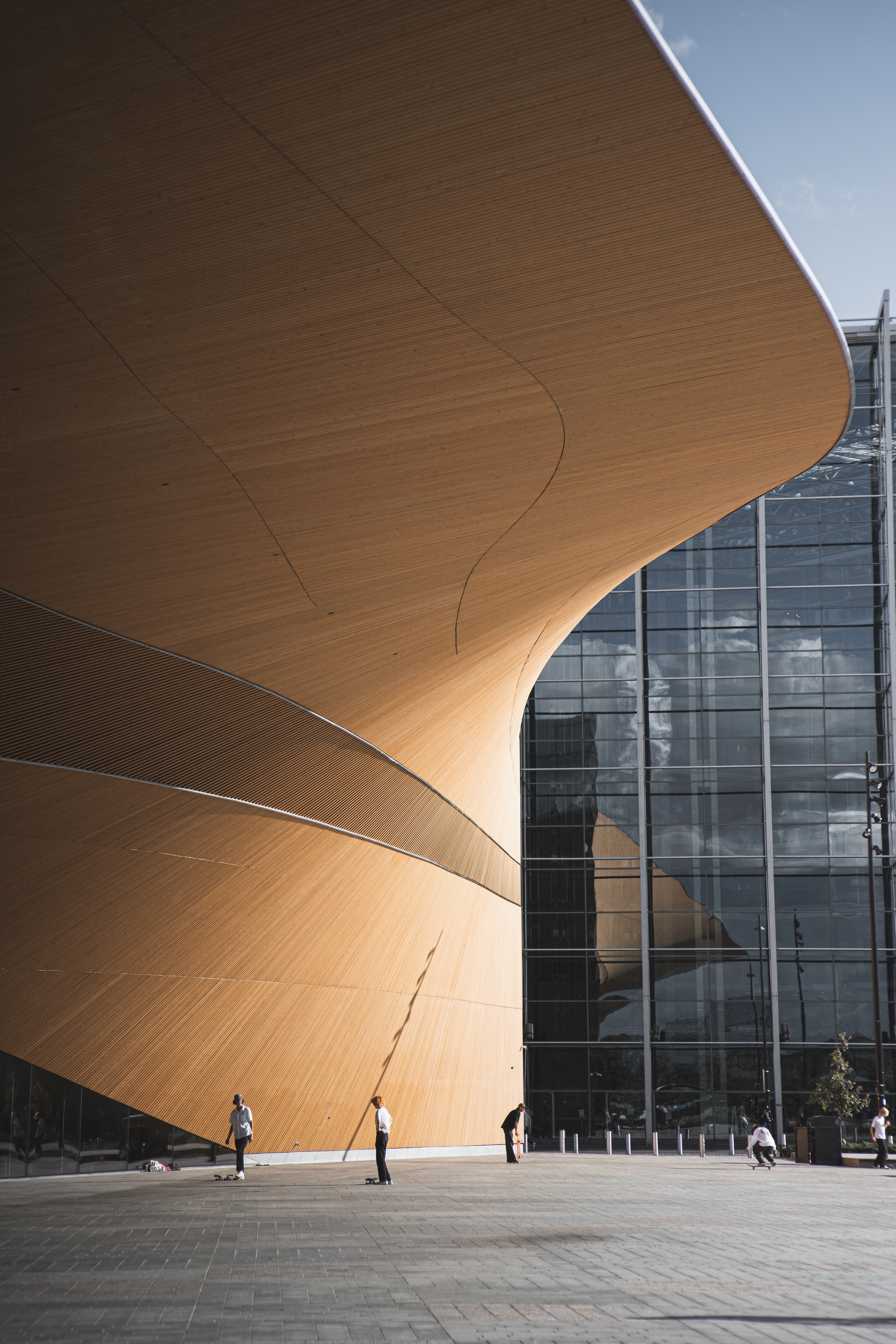 The curving timber underside of the Oodi central library in Helsinki sweeping over the plaza, meeting the building's glass facade.