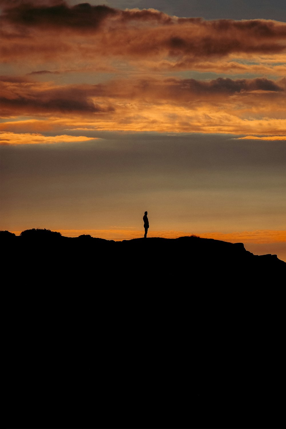 silhouette of person standing on rock formation during sunset