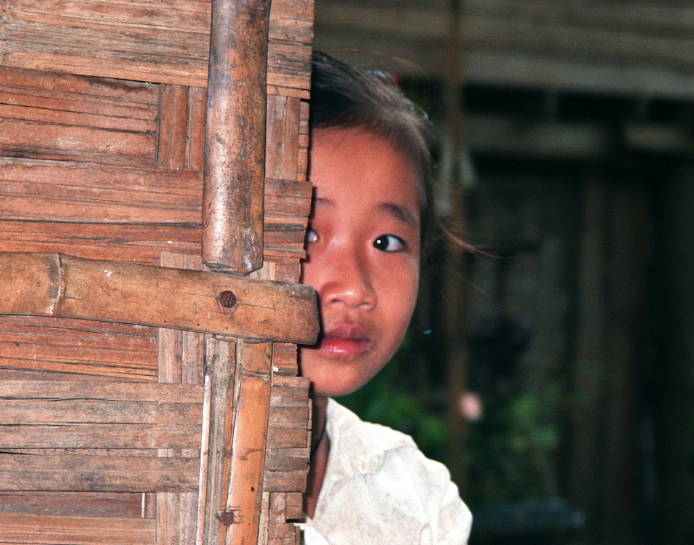 girl in white shirt standing beside brown wooden fence