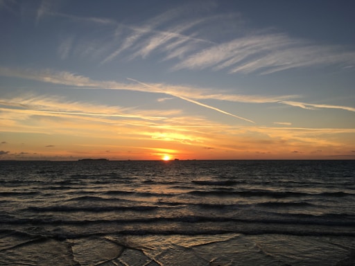 A calming sunset over gentle ocean waves with muted green and blue tones.