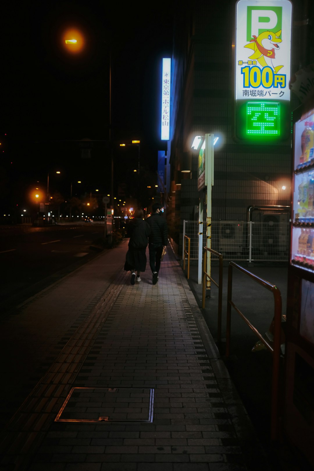 man in black jacket walking on sidewalk during night time