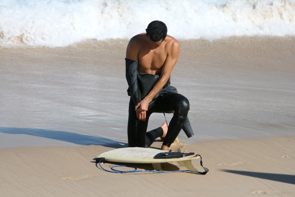 Mann in schwarzer Hose, der tagsüber weißes Surfbrett am Strand hält