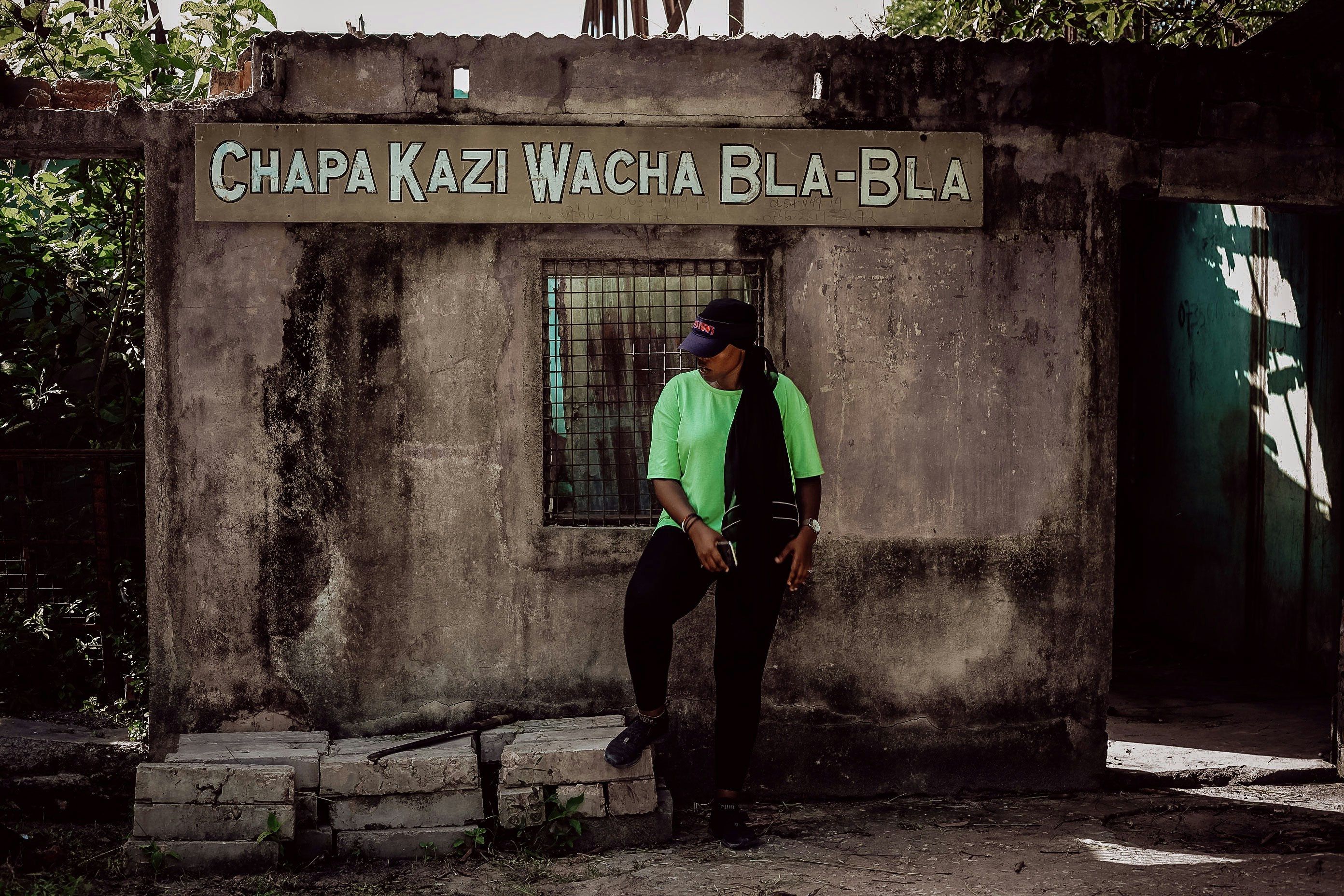 man in green shirt and black pants standing beside gray concrete wall