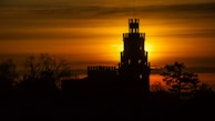 The majestic silhouette of a medieval castle perched on a hill against a sunset sky.