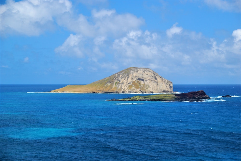 brown and green island on blue sea under blue sky and white clouds during daytime