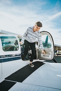 man in gray dress shirt and black pants standing on blue and white car during daytime