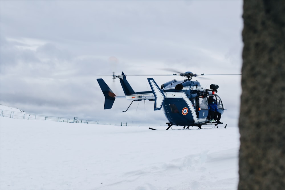 Mann in blauer Jacke fährt tagsüber mit einem blau-weißen Hubschrauber