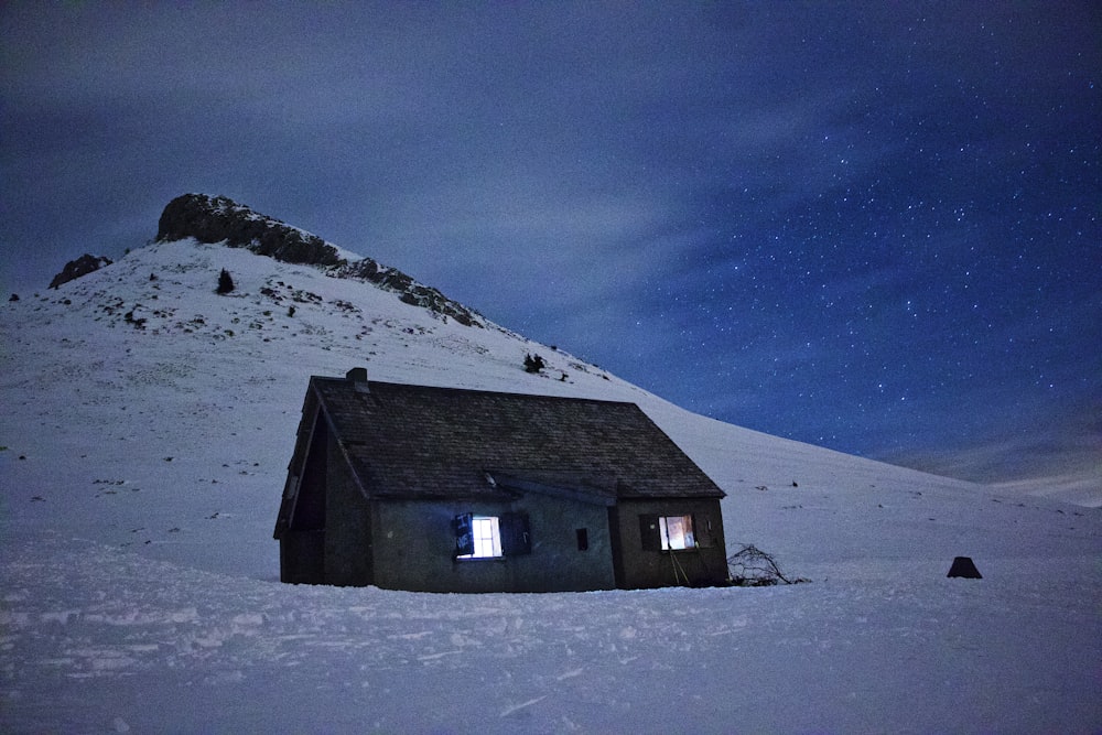 graues Holzhaus auf schneebedecktem Boden unter blauem Himmel tagsüber