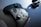 A black gaming controller with colorful buttons labeled X, Y, A, and B is positioned on a flat surface next to wireless earbuds in their charging case. Sunlight casts shadows, emphasizing the controller's sleek design.