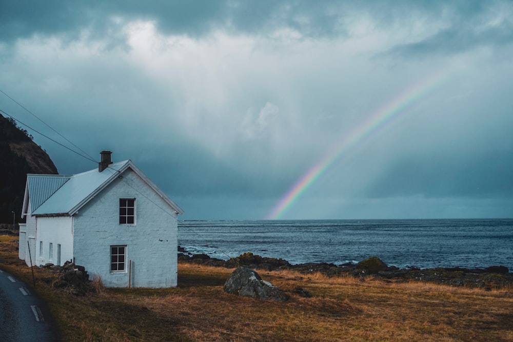 white wooden house near sea under rainbow
