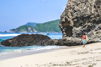 person in red shirt standing on seashore near brown rock formation during daytime