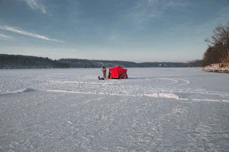 A cozy ice fishing shelter set up on a frozen lake at dawn.