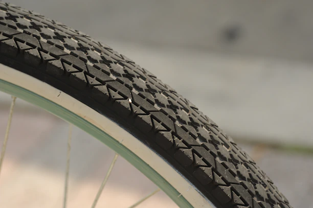 A close-up view of a bicycle tire with a distinctly patterned tread. The tire features a series of geometric shapes arranged in a unique design and is mounted on a metal rim with spokes radiating out.
