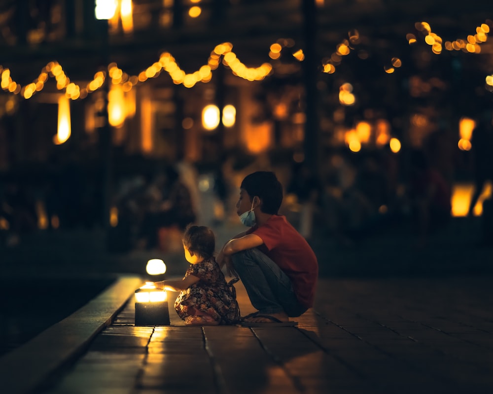 man and woman sitting on sidewalk during night time