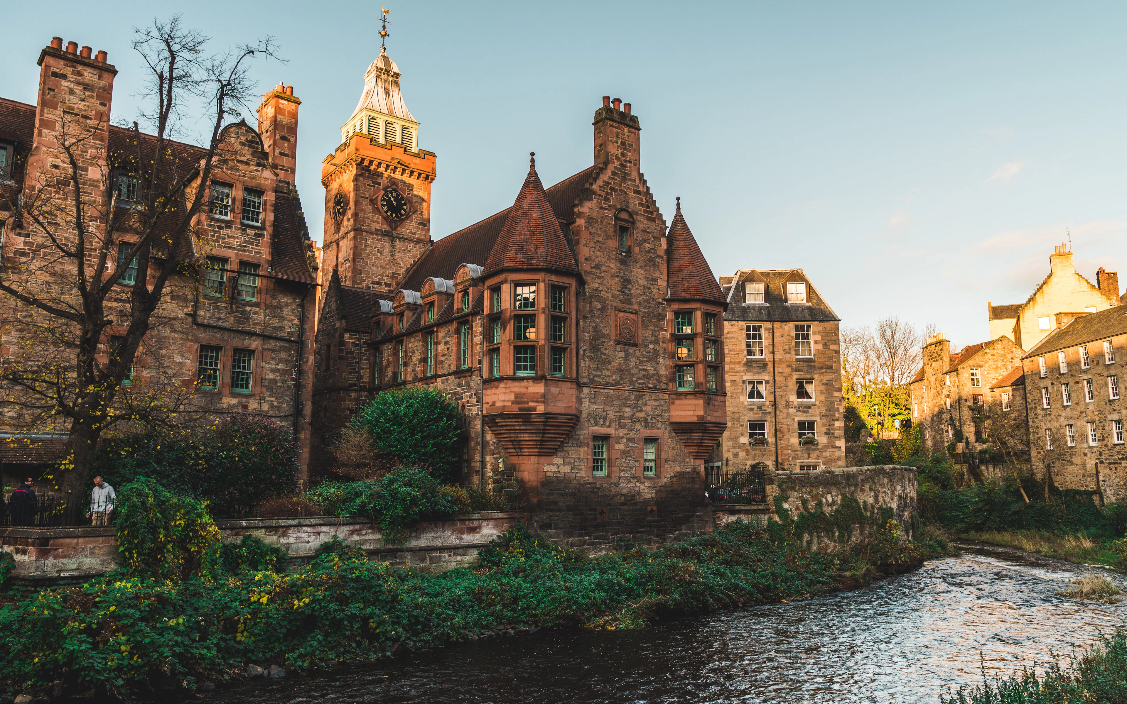 The red sandstone Well Court and its clock tower in Edinburgh's Dean Village, lit by low golden sunlight above the Water of Leith