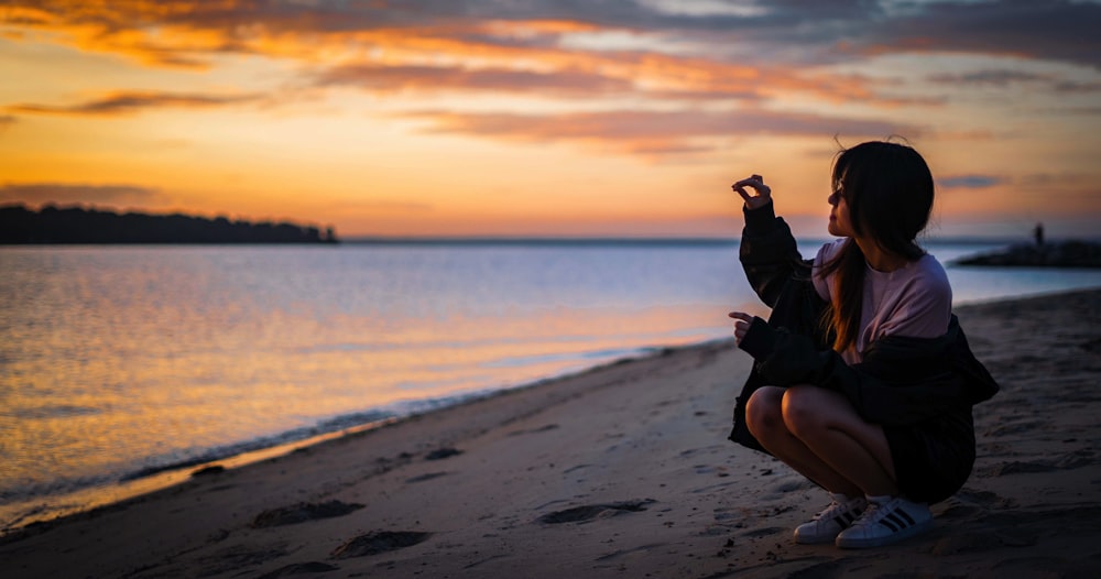 homme en veste noire et pantalon noir assis sur le rivage de la plage pendant le coucher du soleil