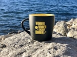 black and yellow ceramic mug on gray rock near body of water during daytime
