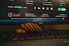 A computer monitor displays a webpage from HelpDesk Heroes, featuring a contact address and email. Social media icons including Facebook, LinkedIn, Twitter, Instagram, and Pinterest are visible. The screen also shows a Trustpilot rating. A stack of cookies is partially visible at the bottom of the image, and part of a keyboard can be seen in the foreground.
