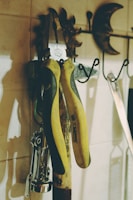 A set of yellow-handled pliers hangs on a rustic wall hook alongside other metal tools and kitchen utensils. The background features a decorative metal sun and moon accent against a tiled wall.