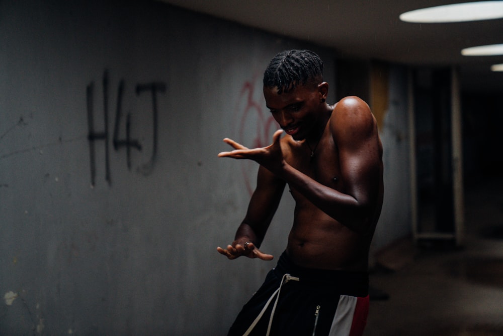 topless man in black and red shorts standing near gray wall