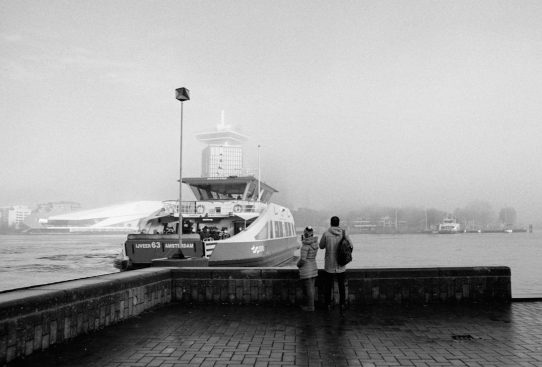 grayscale photo of 2 men standing on dock near body of water