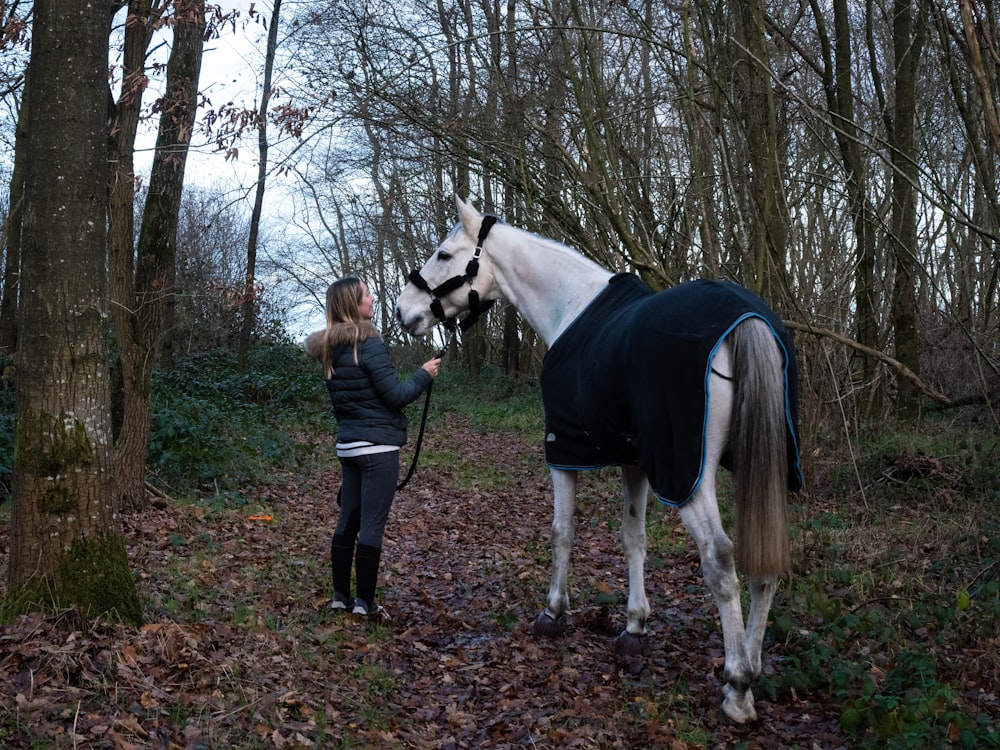 woman in black jacket standing beside white horse during daytime