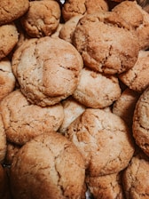 A close-up view of a pile of freshly baked cookies with a golden-brown, crumbly texture. The cookies are stacked on top of each other, showing their rough, homemade appearance.