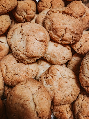 A close-up view of a pile of freshly baked cookies with a golden-brown, crumbly texture. The cookies are stacked on top of each other, showing their rough, homemade appearance.