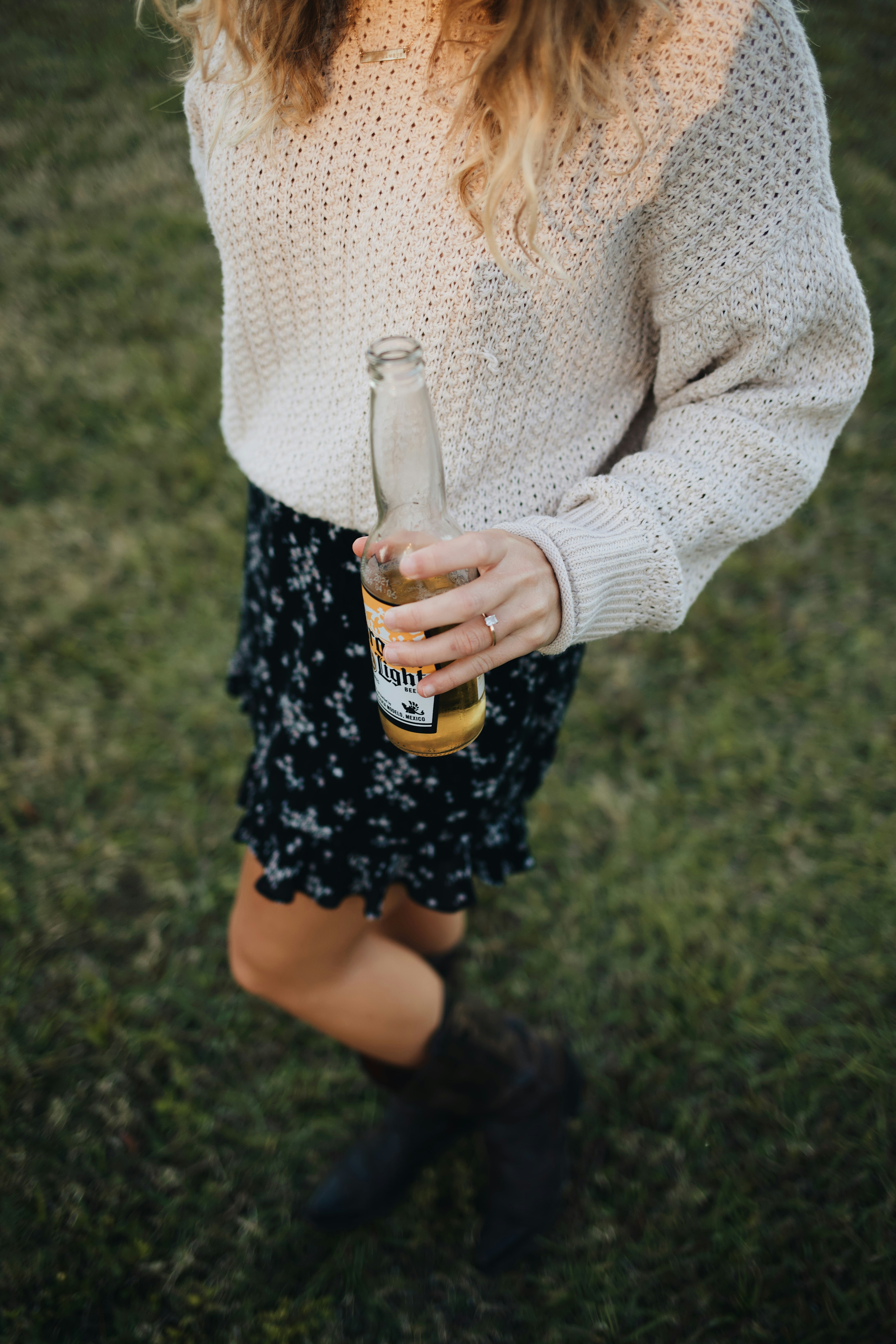 woman in white sweater holding clear glass bottle