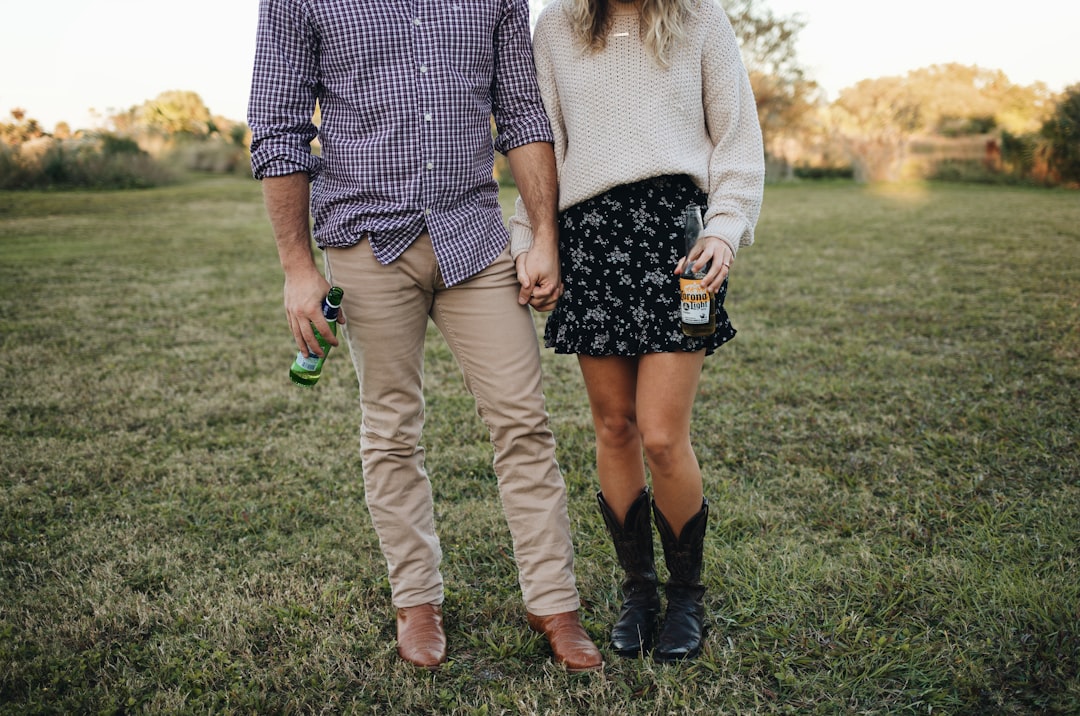 man and woman holding hands while walking on green grass field during daytime