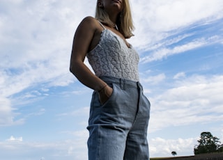 woman in white tank top and blue denim jeans standing on brown field under blue and
