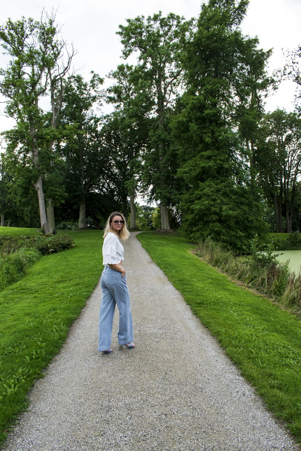 woman in white long sleeve shirt and blue denim jeans standing on gray asphalt road during