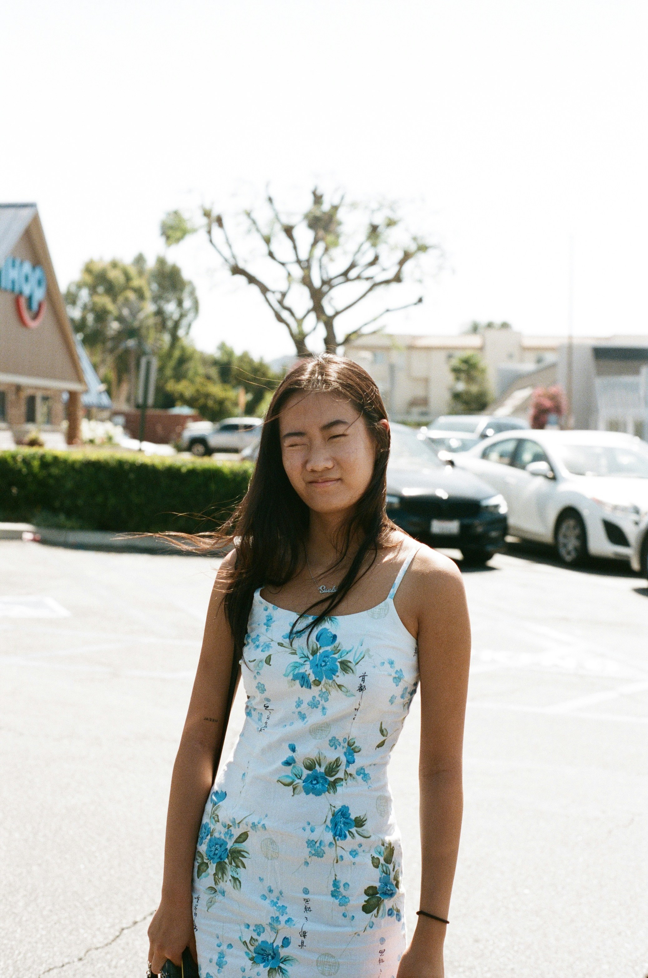 woman in white and blue floral tank top standing on road during daytime