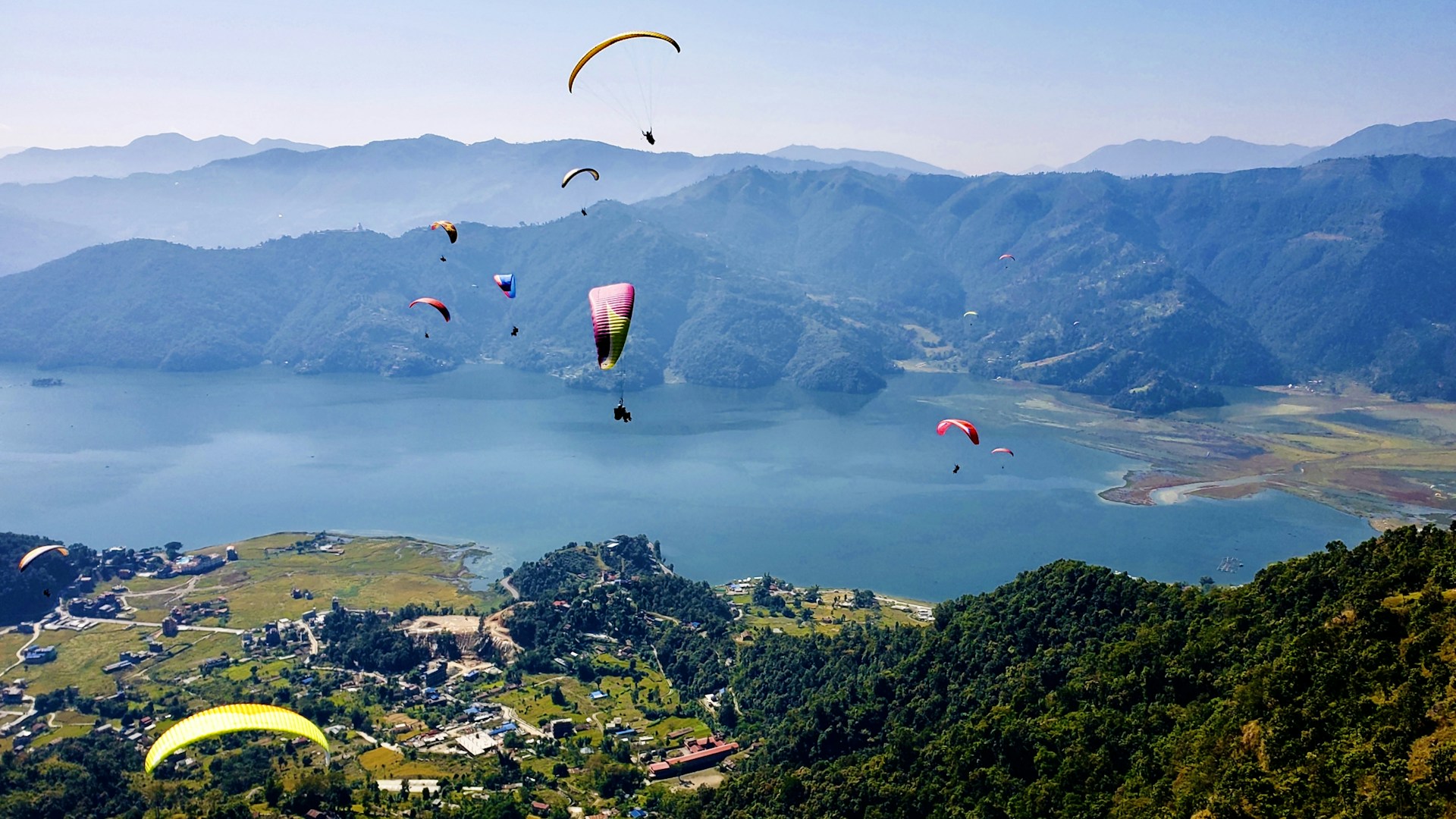 people on parachute over green mountains during daytime