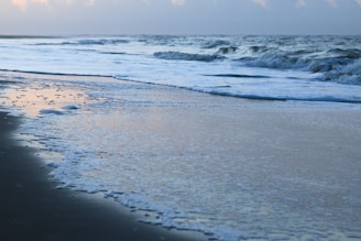 Waves gently rolling onto a sunlit sandy beach at dawn.