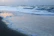 A serene ocean wave gently rolling onto a sandy shore under a soft morning sun.