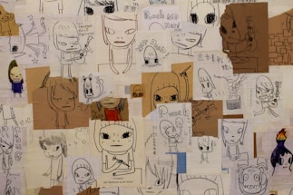 A collage of various doodles and sketches, primarily depicting cartoonish characters with large eyes. Some characters are holding musical instruments like guitars. Handwritten text appears throughout, with phrases such as 'This machine kills fascists' and 'Punch me hard.' The doodles are on different pieces of paper, some colored and some plain, layered over each other.