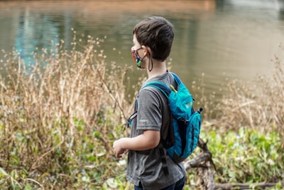 boy in blue and black backpack standing near body of water during daytime