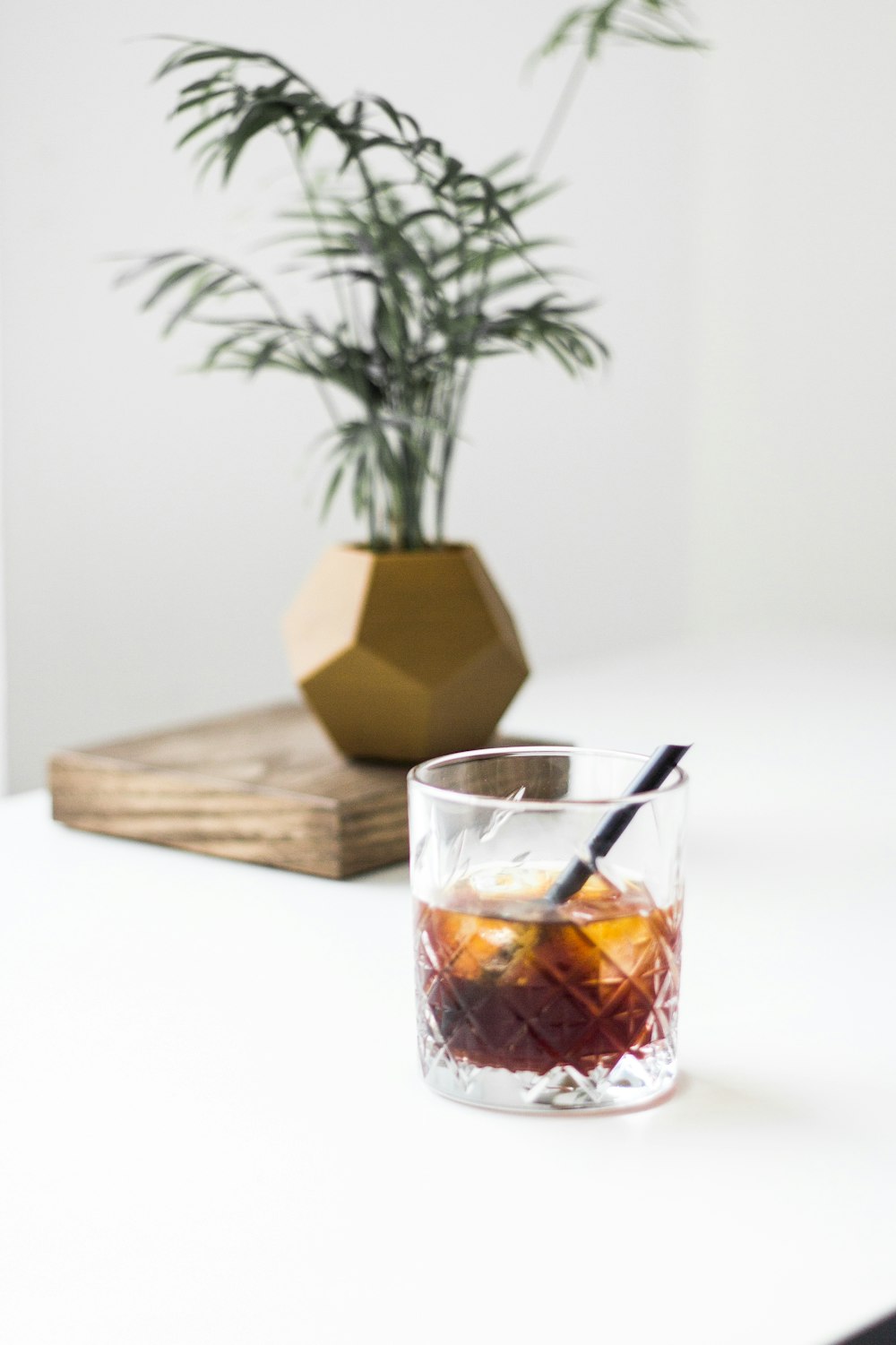 clear drinking glass with brown liquid inside beside brown wooden chopping board