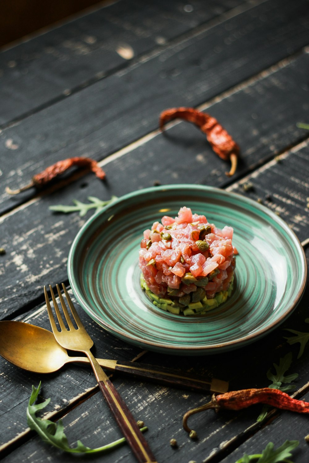 red and green round food on green ceramic plate beside silver fork and knife