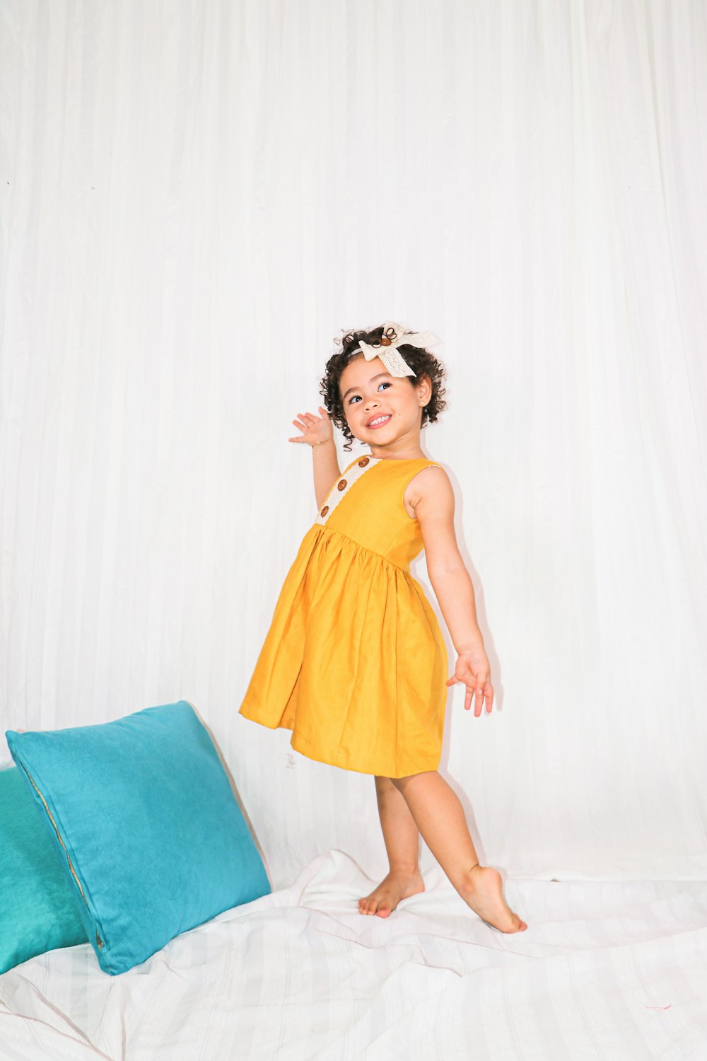 girl in yellow sleeveless dress standing beside blue bed