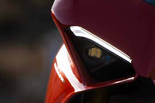 Close-up of a sleek red motorcycle headlight glowing softly in a dark setting