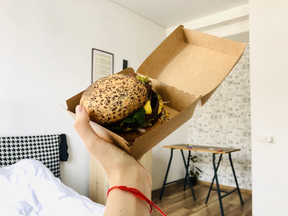 person holding burger with lettuce and cheese