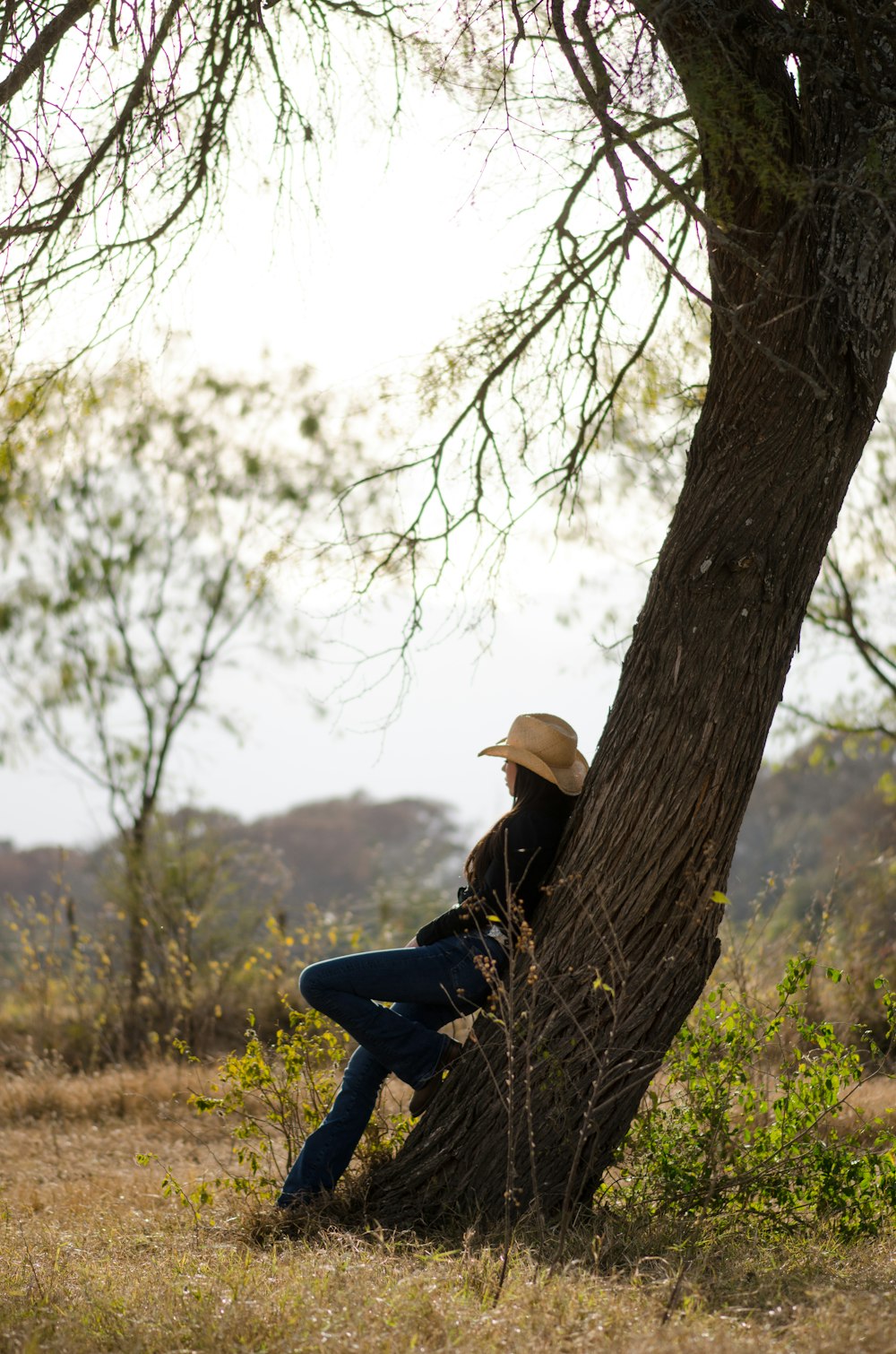 낮 동안 나무 줄기에 앉아 있는 파란색 재킷과 갈색 모자를 쓴 여자