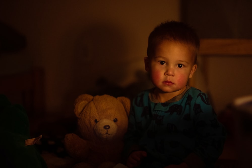 boy in blue and white shirt beside brown bear plush toy
