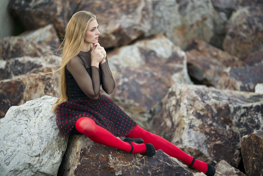 woman in black sleeveless dress sitting on gray rock