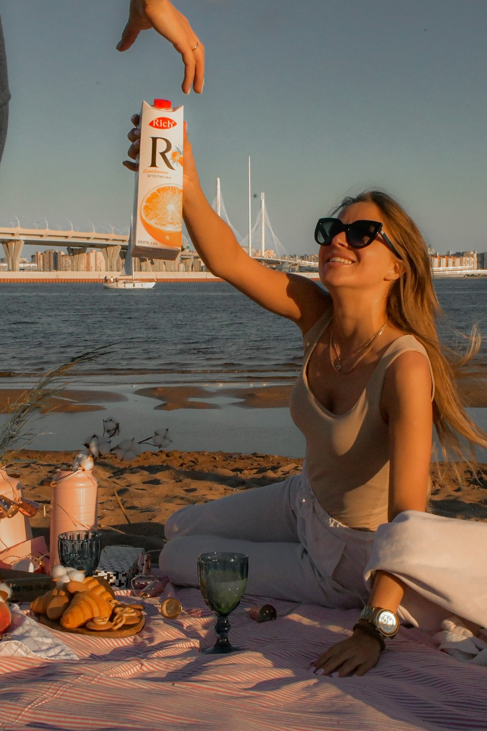 woman in white tank top and white pants sitting on beach during daytime