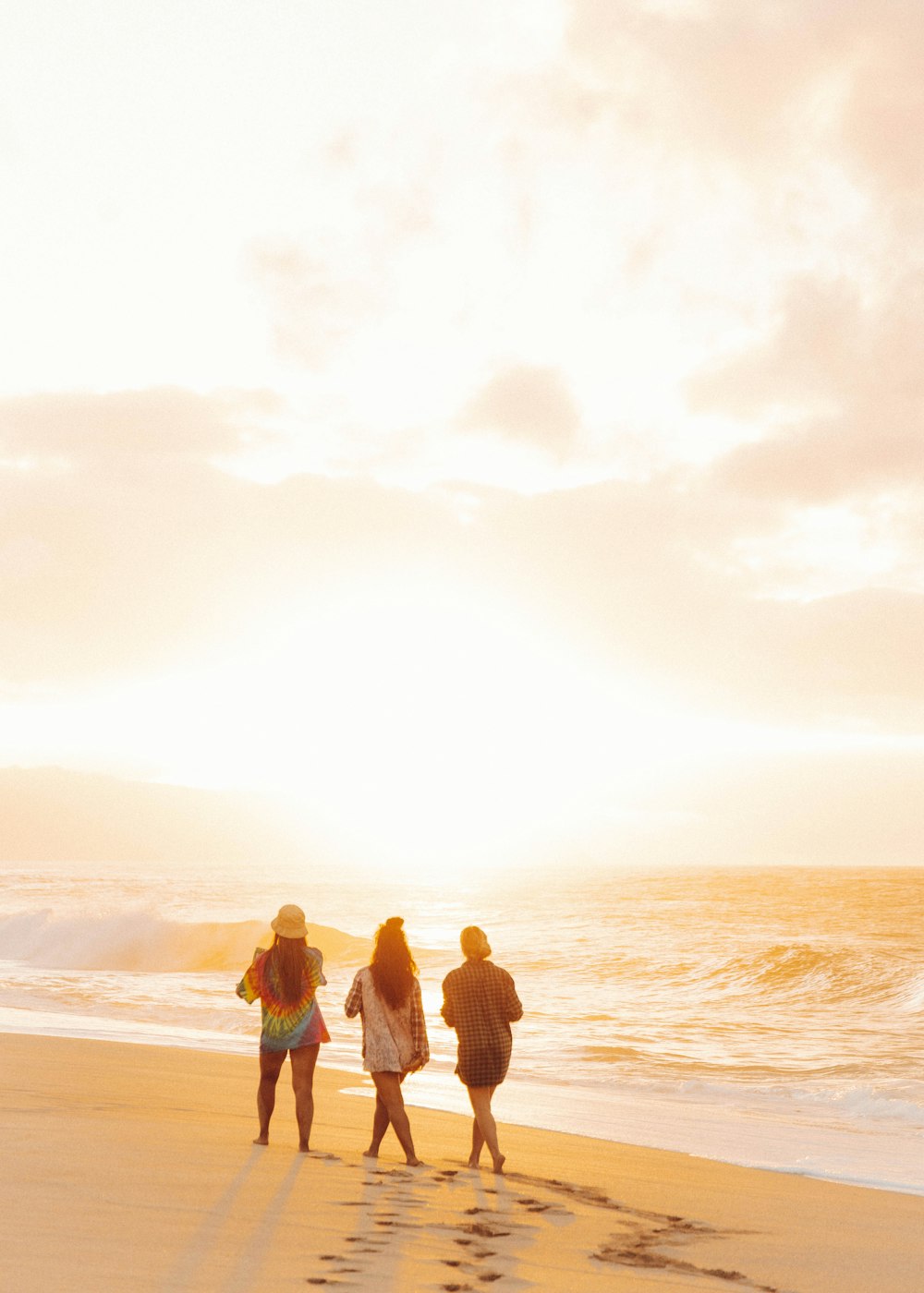 일몰 동안 해변에 서 있는 3명의 여성과 남성