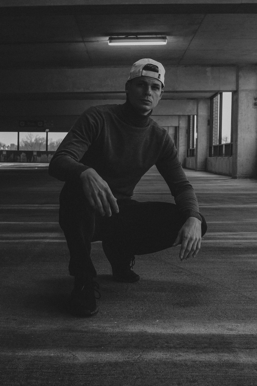 man in black long sleeve shirt and pants sitting on road in grayscale photography