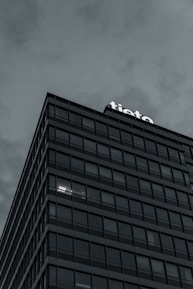 A modern multi-story building with a grid-like facade, displaying the word 'tieto' at the top. The overcast sky adds a moody atmosphere. The building's windows reflect the subdued light, with some illuminated from within.